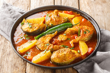 Machher jhol or machha jhola, is a traditional spicy fish curry in Bengali and Odia cuisines closeup on the plate on the wooden table. Horizontal - obrazy, fototapety, plakaty