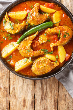 Bengali Fish Curry Macher Jhol with potatoes closeup on the plate on the wooden table. Vertical top view from above