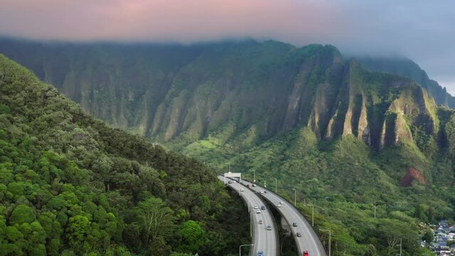 Scenic route on Oahu Hawaii island at golden sunrise. Interstate H3 passing through majestic green Koolau Mountains with Trans-Koolau twin tunnels. Aerial along highway with epic nature landscape view