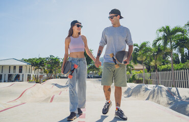 Young happy couple with skateboards enjoy longboarding at the skatepark