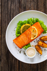 Seared salmon steak with baked potatoes and fresh vegetable salad served on wooden table

