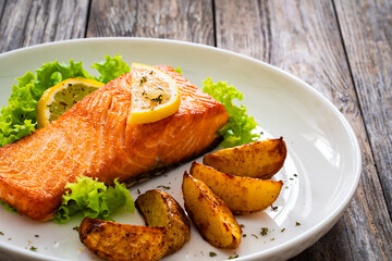 Seared salmon steak with baked potatoes and fresh vegetable salad served on wooden table
