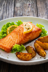 Seared salmon steak with baked potatoes and fresh vegetable salad served on wooden table
