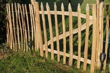 Bieger Gartenzaun aus Holz auf grüner Wiese im Garten bei Sonne am Abend im Spätsommer