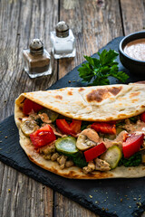 Italian piada wraps - piadina filled with mozzarella cheese, fried pork and vegetables and on wooden table
