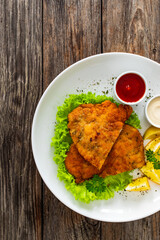 Crispy breaded seared chicken cutlet with lemon slices and fresh vegetables on wooden table
