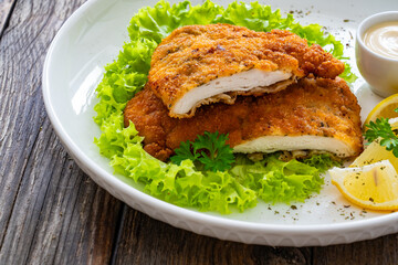 Crispy breaded seared chicken cutlet with lemon slices and fresh vegetables on wooden table
