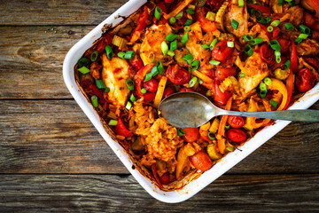 Jambalaya one pot dish - fried chicken breasts with white rice, tomatoes, bell pepper and celery on wooden table
