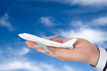 A man's hand holds a model of a passenger airliner against the background of a sky with clouds.