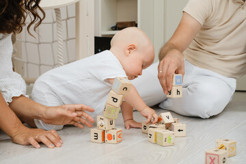 Child early development. Parents building from wooden cubes on the floor, learning shapes, letters,...