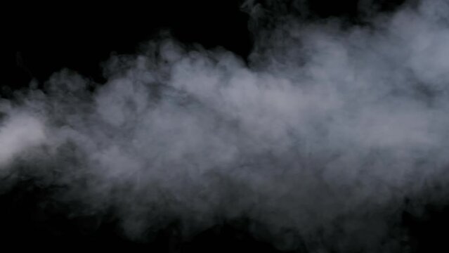 Jet stream of smoke or vapor on black background in slow motion 4K. Explosion steam. White smoke clouds rise up. Floating fog. Real atmospheric effect, abstract particles of smoke texture. Copy space