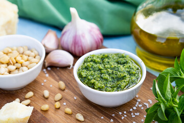 ingredients for the preparation of pesto sauce. basil, pine nuts, garlic, basil, parmesan on a blue table and wooden board, close-up