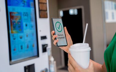 Young woman paying for coffee at vending machine using contactless method of payment 