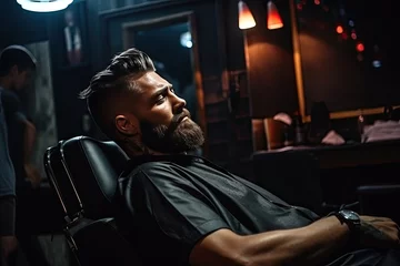 Poster Handsome young man in a barber's chair getting a stylish haircut and beard trimmed by an experienced barber in a modern barbershop. © Iryna