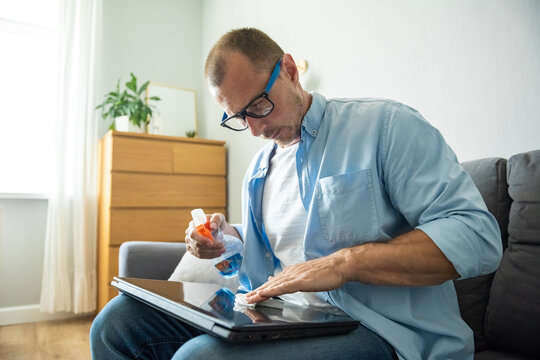 Laptop cleaning up. Cleaning accessories: brush, cloth, spray. Computer monitor, display care. Man who wipe laptop at home