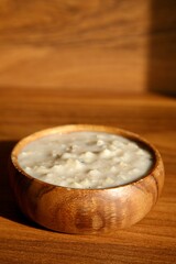 Oatmeal in a wooden bowl on a wooden background in the morning sunlight - 655127581