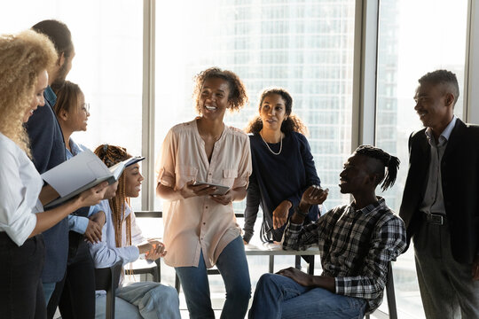 Happy diverse colleagues chatting at corporate meeting in modern office, smiling African American employees coworkers discussing project strategy, sharing ideas, involved in team building activity