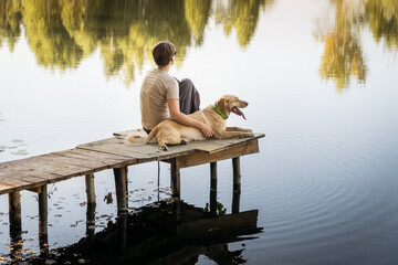 Female with a labrador dog on a wooden fishing bridge enjoying peaceful warm water view.