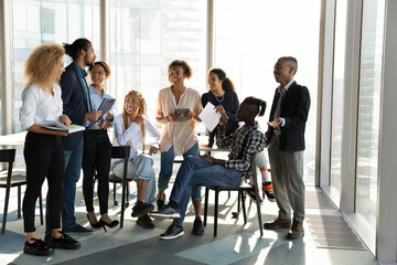 Happy diverse colleagues having fun at briefing, chatting, discussing project strategy or sharing...