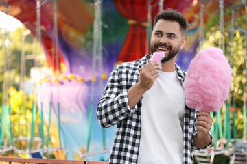 Happy young man eating cotton candy at funfair, space for text