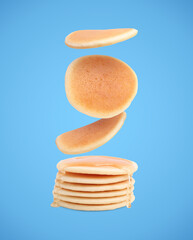 Many tasty fresh pancakes falling on light blue background