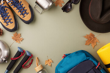 Hiking for a seasonal rendezvous with the palette of fall. Top view flat lay of different camping equipment, trendy hat, dry fallen leaves on pastel green background with advert space