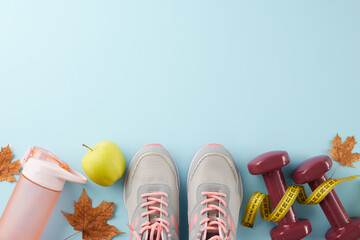 Autumn fitness transition idea. Top view photo of dumbbells, fresh apple, tape measure, stylish shoes, bottle, dry maple leaves on light blue background with advertising area