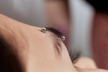 Professional placing the jewel of piercing on the temple on the head with ball. Tragus type.