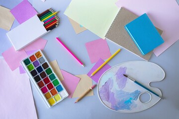 Back to school, watercolor paints, brushes and colored pencils, palette, school supplies on a gray background, top view 
