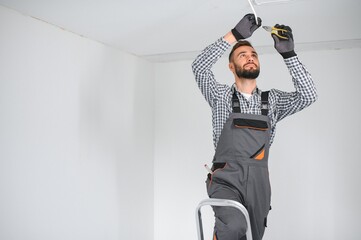 Young electrician installing smoke detector on ceiling.