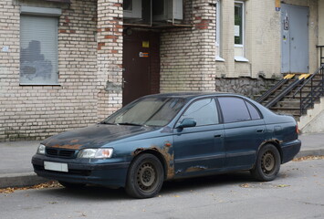 An old broken dark blue car stands near the brick wall of a residential building, Iskrovsky Prospekt, Saint Petersburg, Russia, September 29, 2023