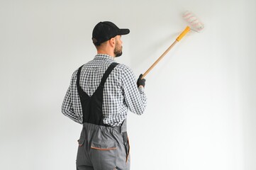 Young worker painting wall in room.