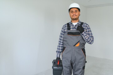Obraz premium profession, construction and building - happy smiling indian worker or builder in helmet over grey background.