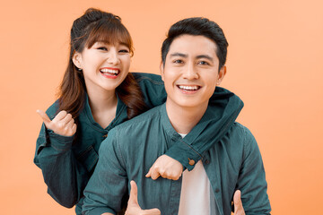 Portrait of a happy young couple hugging while standing and showing thumbs up gesture over yellow wall