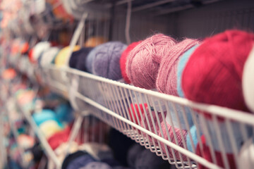Colorful wool yarn balls on shelf in knitting shop, shallow depth of field