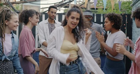 Slow motion portrait of beautiful young woman dancing outdoors at street party with diverse group of friends. Youth culture and leisure activity concept.