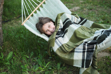 Nestled in a hammock, a joyful girl wrapped in a blanket illustrates serenity, her garden a...