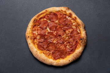 Pepperoni pizza on dark black background with copy space. Neapolitan pizza with salami and tomato sauce