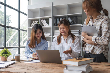 Asian College groups of students using laptop, tablet, studying together with notebooks documents paper for report near windows in classroom. Happy young study for school assignment, Soft focus