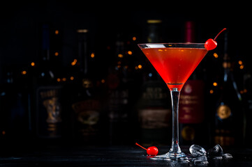 Manhattan cocktail drink with bourbon, red vemuth, bitter, ice and cherry in glass, dark bar counter background, bar tools and bottles