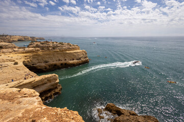 Obraz premium Benagil, Portugal - September 8th, 2023: South coast of Portugal, cliff, caves, beaches, sand, sea, waves, trail, kayaks, motorboats, sailboats