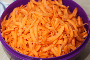 Grated carrot in plastic violet bowl background. Vegetable salad texture. Vibrant orange color....