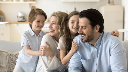 Loving parents spend carefree time together at home with little 6s kids. Pretty children hugging mom and dad show bond and affection feel happy, enjoy sweets moment. Family love, childcare, custody