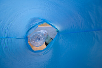 Detail of a volunteer's hand putting a plastic bottle in the bag. Photo taken from below. Concept...