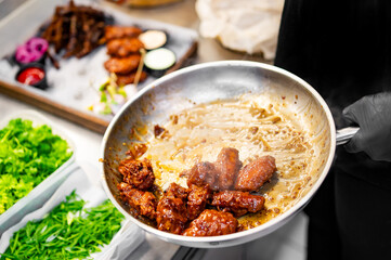 chef cooking chicken wings in a sauce on pan in the kitchen