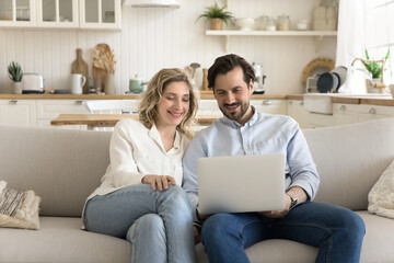 Young attractive spouses watch movie on computer at home, rest on couch, look at laptop screen,...