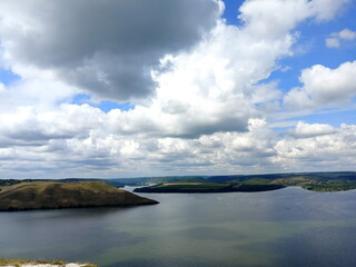 Panorama from above of the smooth water surface of the Dniester bypassing the small green islands against the background of the blue semi-cloudy sky.