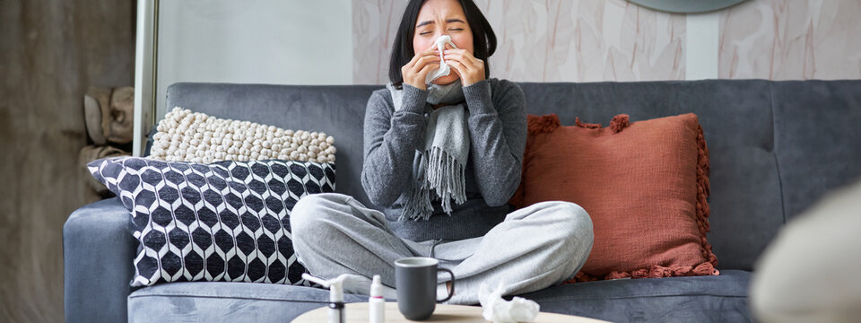 Young Asian Woman Staying At Home, Feeling Unwell, Catching A Cold, Sick Leave, Sneezing, Drinking Hot Tea And Taking Medication