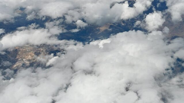 Aerial view through the airplane window of the mountainous region of Peru. Lots of clouds, mountains and little vegetation in a brown setting.