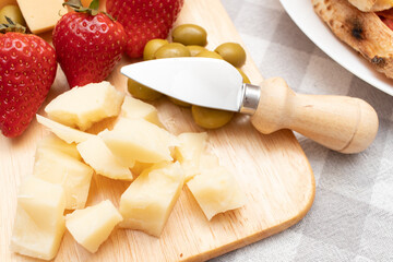 A plate of assorted cheese, strawberries, green olives and a cheese knife